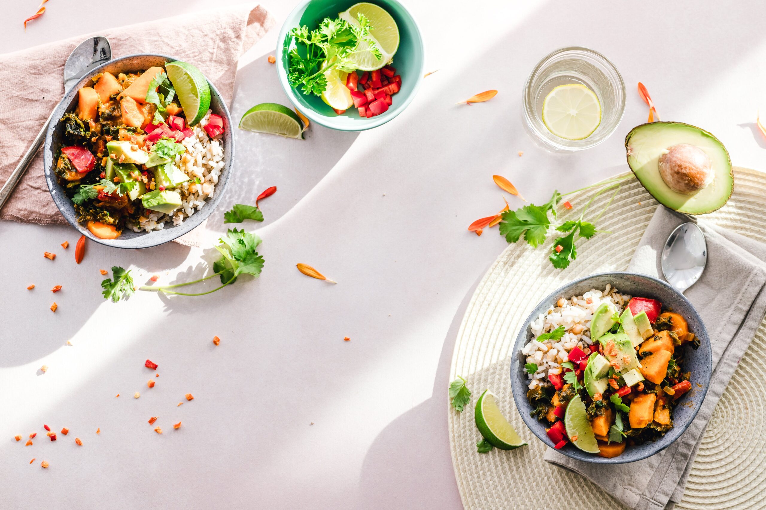 Bowl of plant-based food including grains, vegetables and beans on a table with avocado and lime wedges